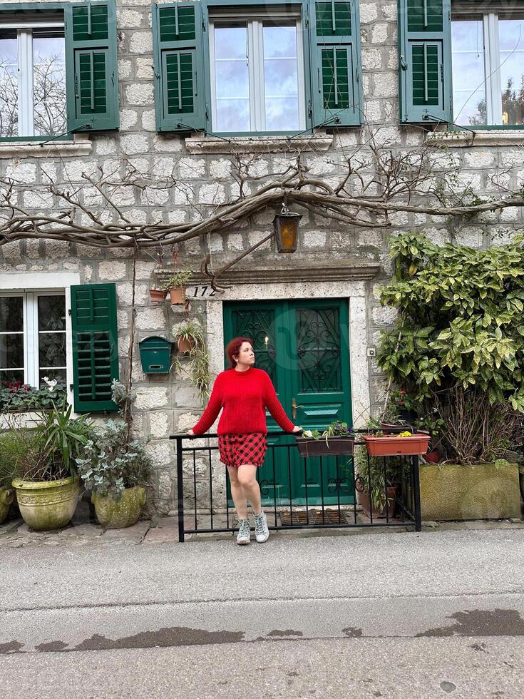 Charming stone building with green shutters and millennial woman in red standing in front. a picturesque scene capturing the essence of rustic architecture and fashion. Travel and journey concept photo