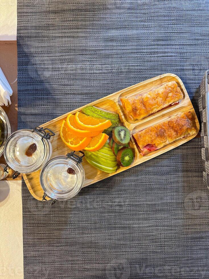 colorful breakfast spread showcases sliced fruits and pastries on a wooden tray, offering a vibrant start to the day. accompanied by glasses of water, this arrangement exudes freshness and simplicity. photo