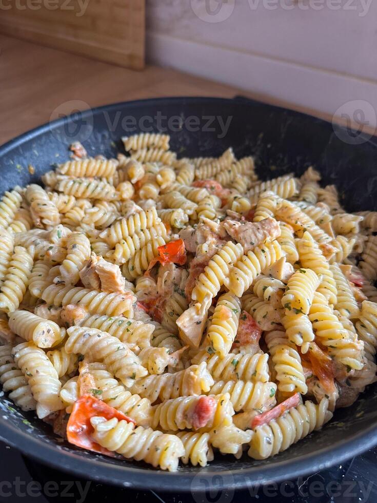 Delicious bowl of creamy rotini pasta mixed with pieces of chicken and vibrant vegetables is served fresh and ready to eat. photo