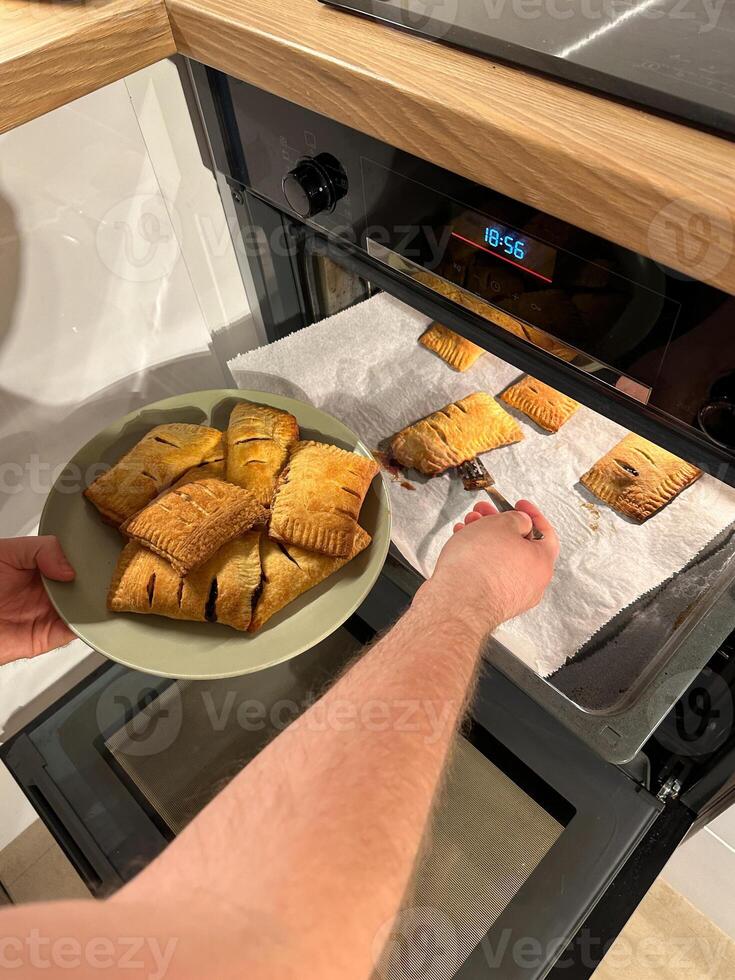 Freshly baked pastries are being taken out of the oven, steaming and golden brown, ready to be served on a green plate. Aroma of crispy dough fills the cozy kitchen photo