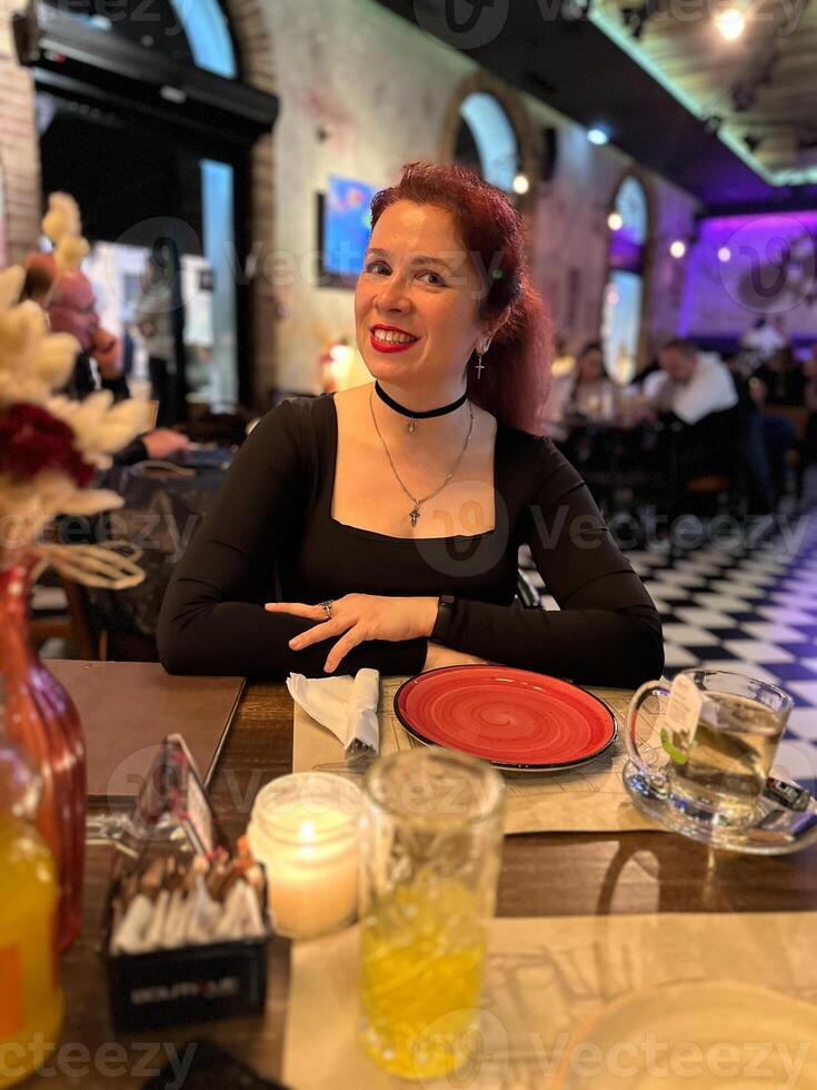 Millennial woman enjoying a pleasant evening at a lively restaurant, seated at a table with a red plate and warm candlelight. Atmosphere is night with a mix of modern and cozy interior design, photo