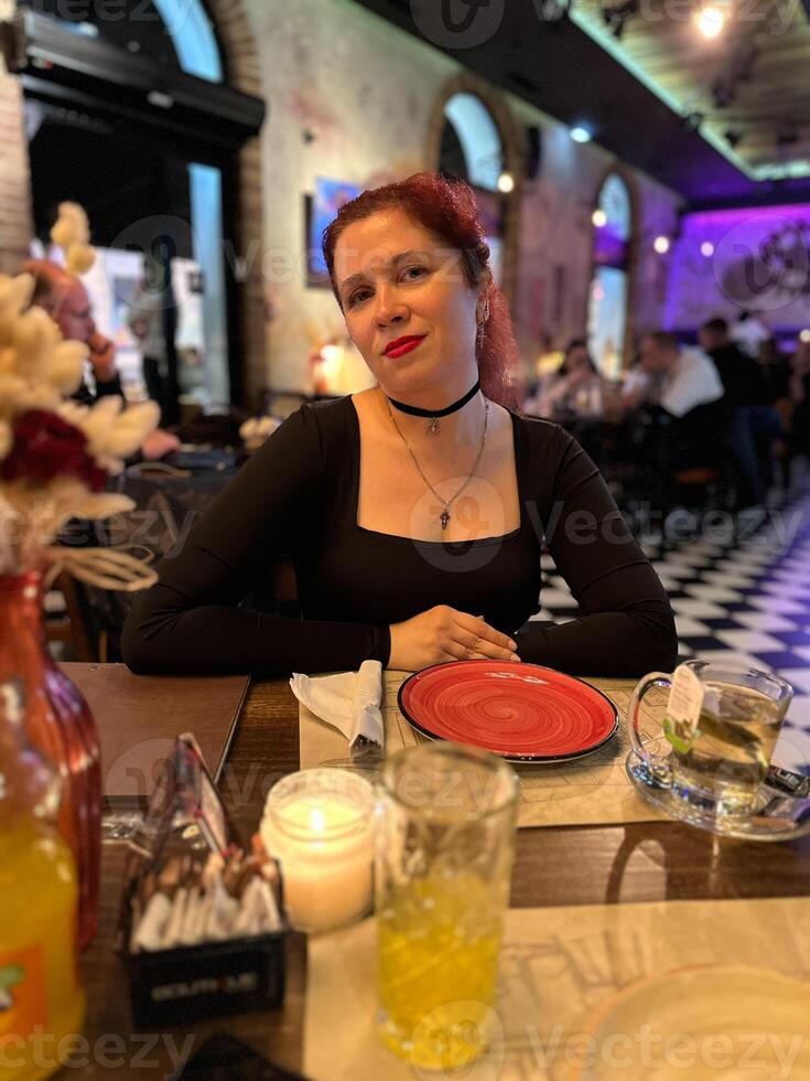 Millennial woman enjoying a pleasant evening at a lively restaurant, seated at a table with a red plate and warm candlelight. Atmosphere is night with a mix of modern and cozy interior design photo