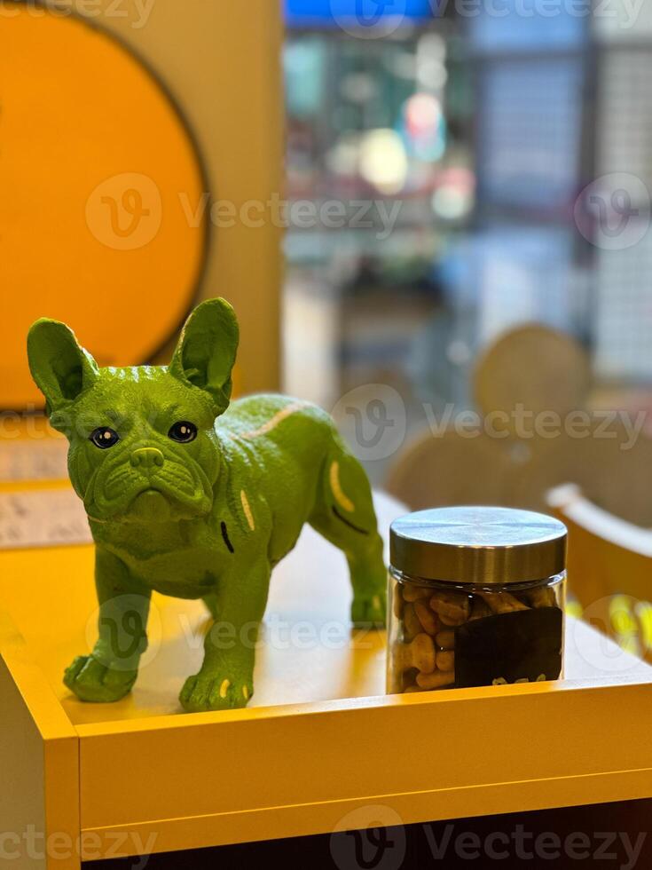 Vibrant green dog statue stands elegantly on a yellow shelf beside a jar of treats. Treats for pet dogs photo