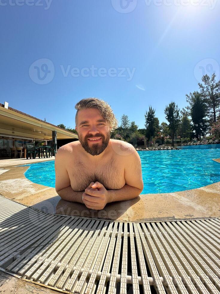 Millennial man taking selfie by swimming pool. Vibrant blue water and relaxed setting create a perfect atmosphere for summer fun. Holidays and vacation photo
