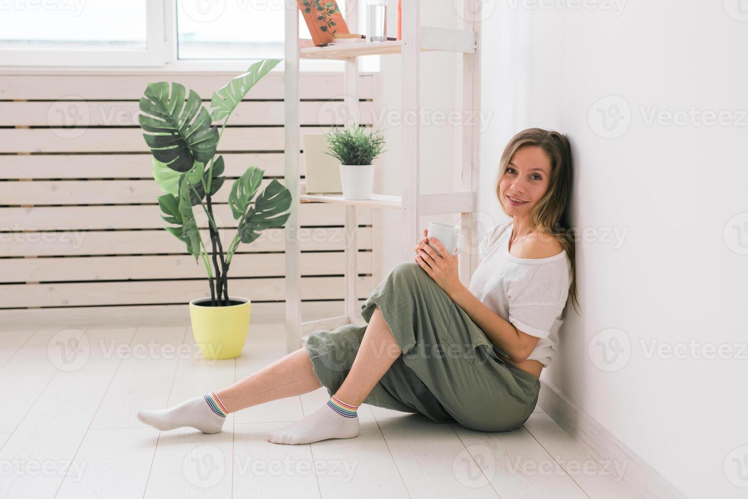 Dreaming girl sitting on floor at home and drink tea from cup. photo