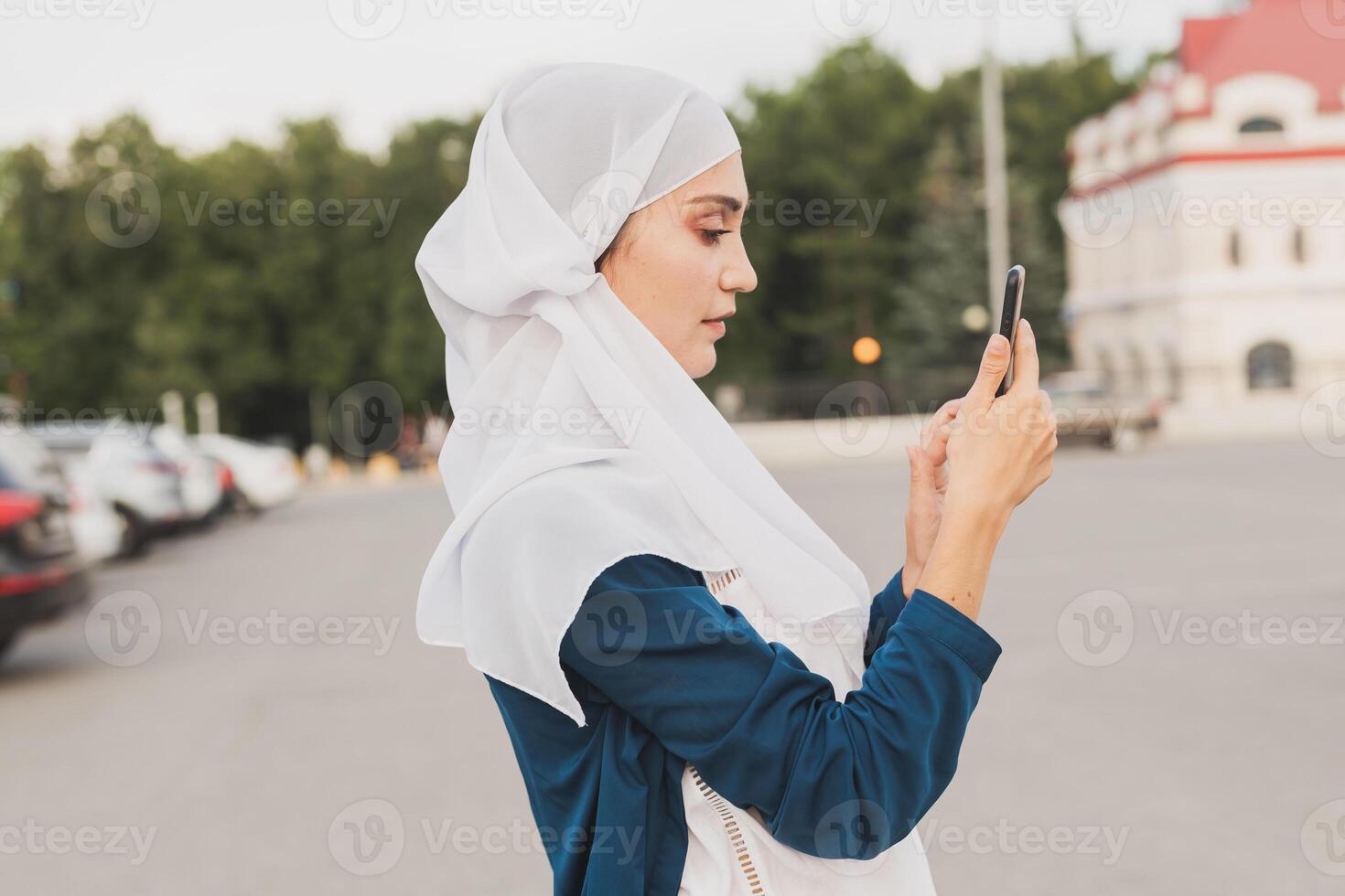 Muslim young woman wearing hijab head scarf in city texting cell phone photo
