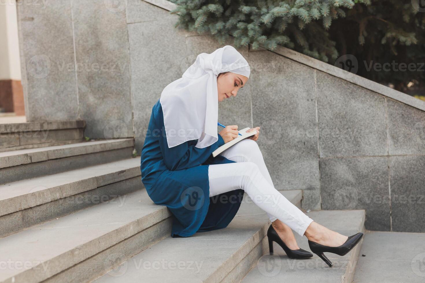 Female middle eastern college student sits on stairs in university campus. Education and knowledge concept. photo