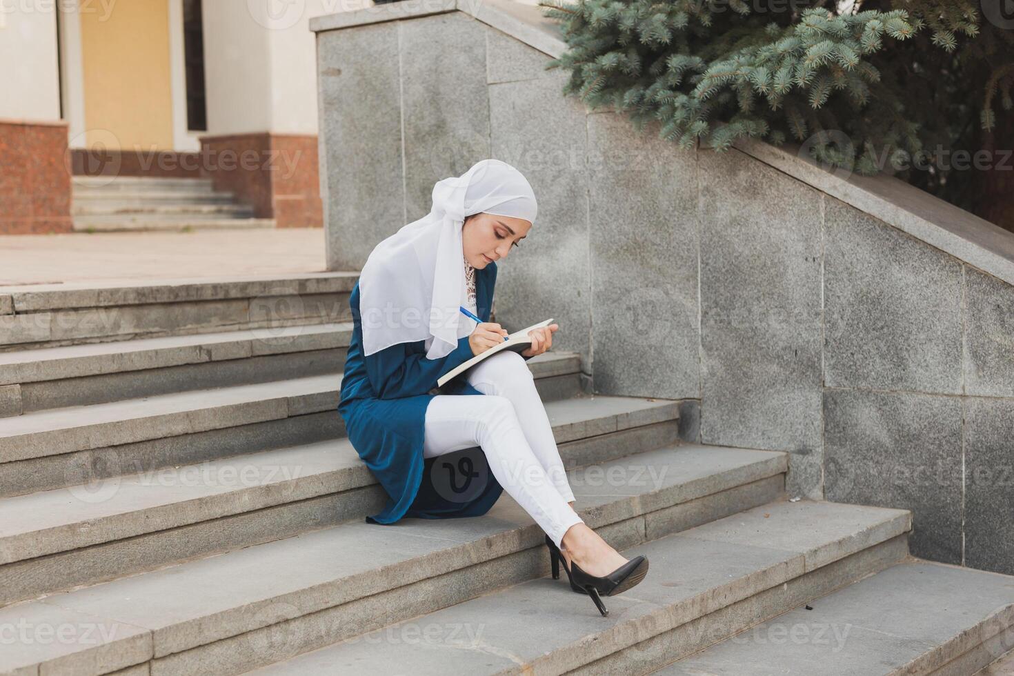 Female middle eastern college student sits on stairs in university campus. Education and knowledge concept. photo