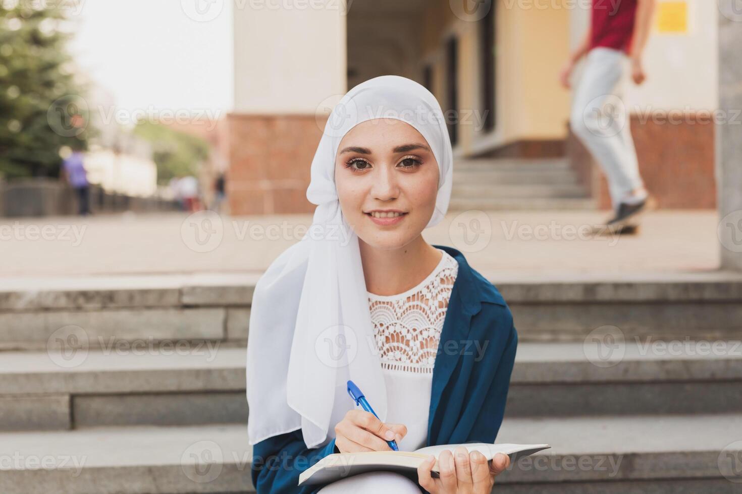 Female middle eastern college student sits on stairs in university campus. Education and knowledge concept. photo