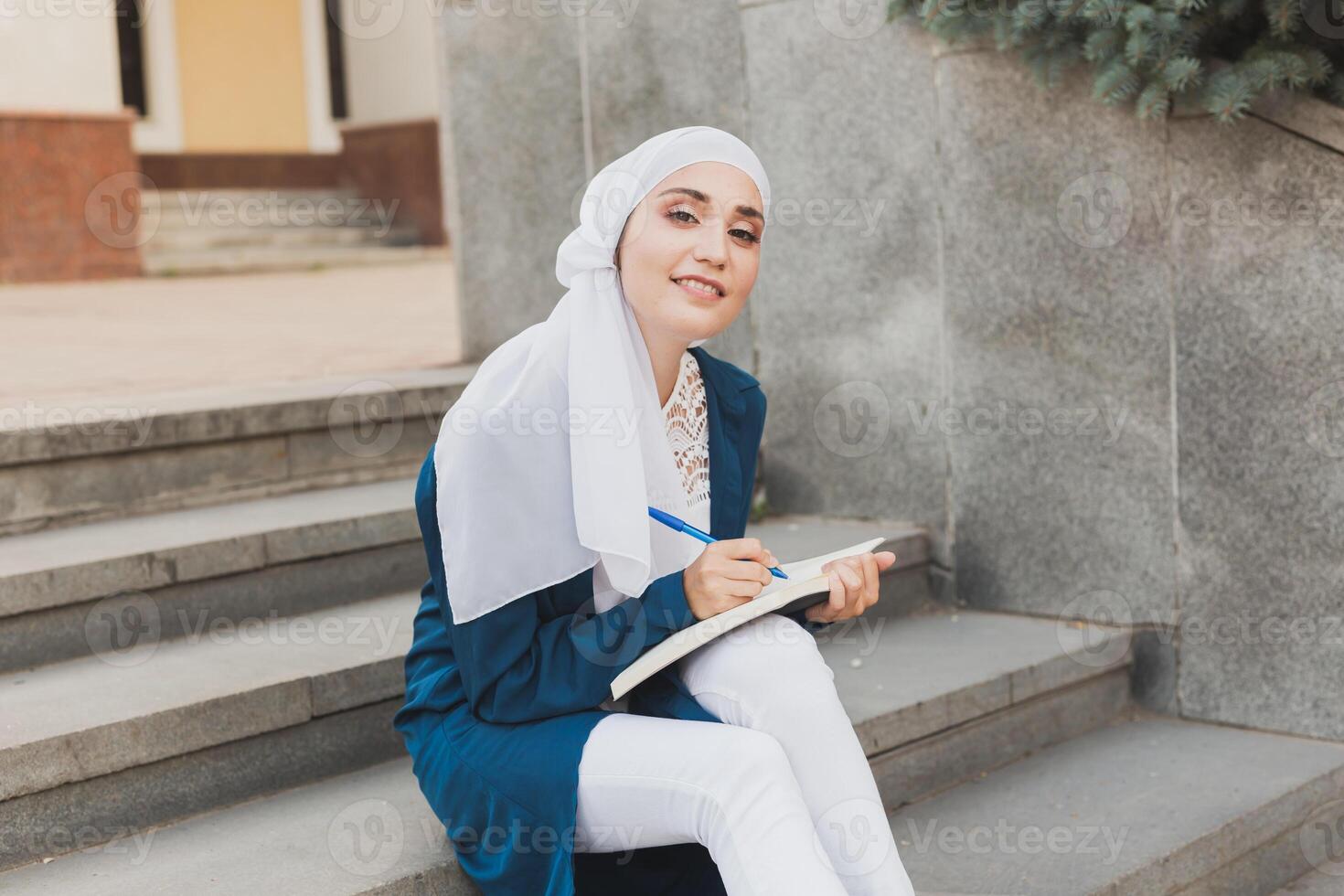 Female middle eastern college student sits on stairs in university campus. Education and knowledge concept. photo