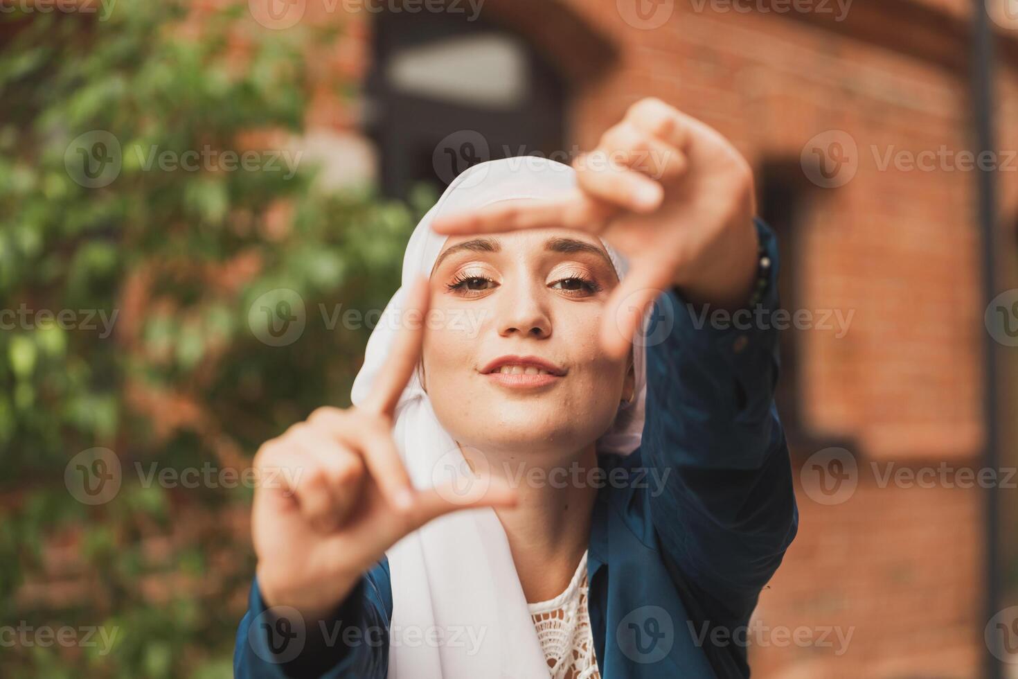 Portrait of young muslim girl making a camera frame with fingers outdoors. photo