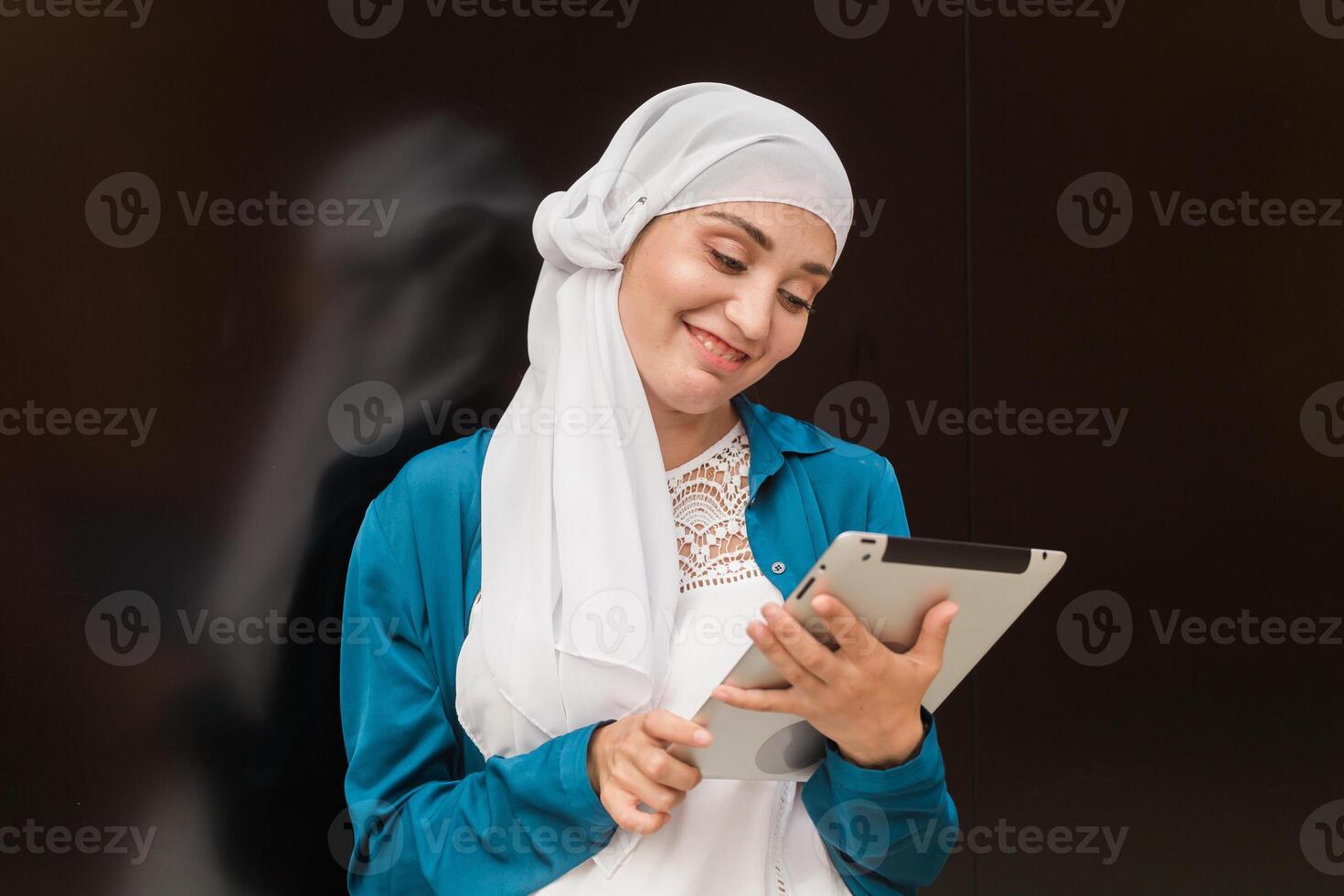 Smiling muslim girl using digital tablet, browsing Internet or social networks outdoor photo