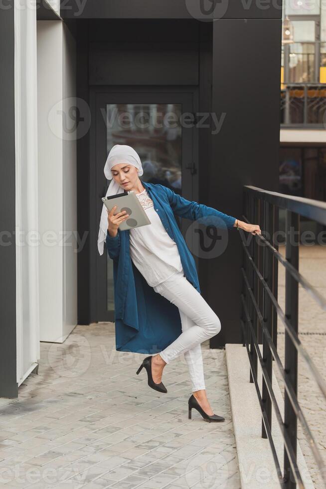 Smiling muslim girl using digital tablet, browsing Internet or social networks outdoor photo
