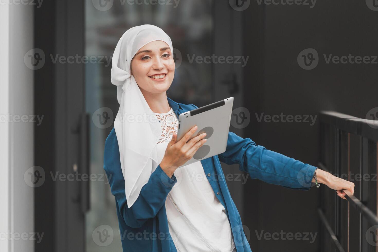Smiling muslim girl using digital tablet, browsing Internet or social networks outdoor photo