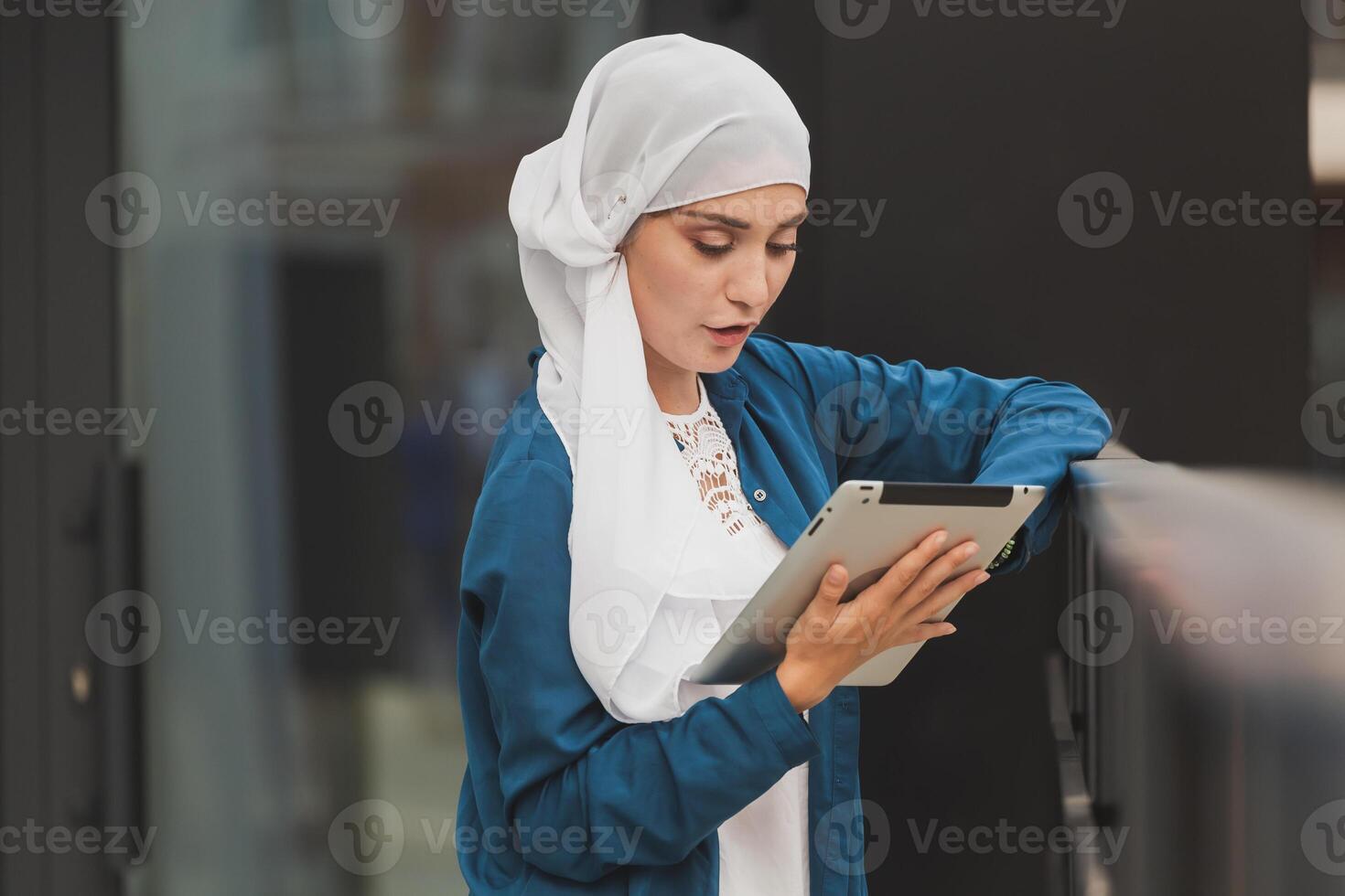 Smiling muslim girl using digital tablet, browsing Internet or social networks outdoor photo