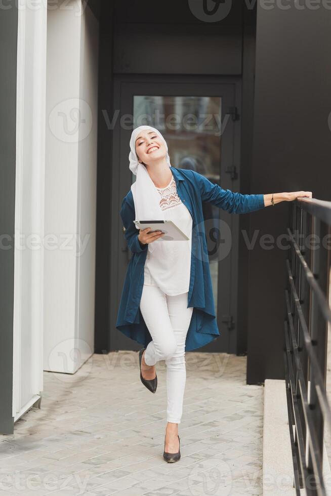 Smiling muslim girl using digital tablet, browsing Internet or social networks outdoor photo