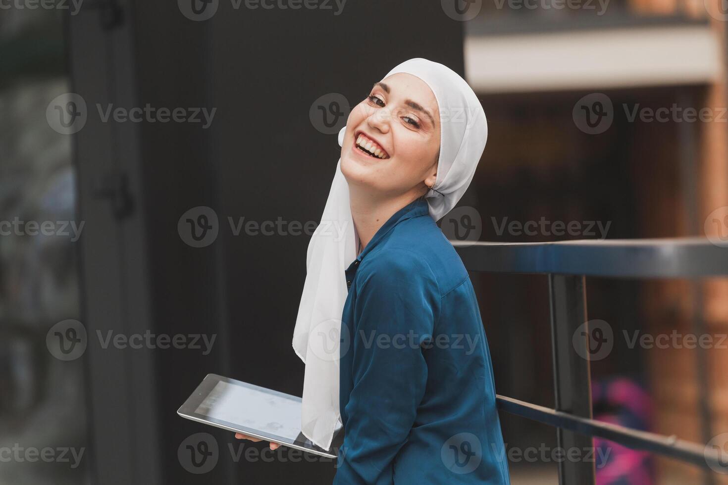 Smiling muslim girl using digital tablet, browsing Internet or social networks outdoor photo