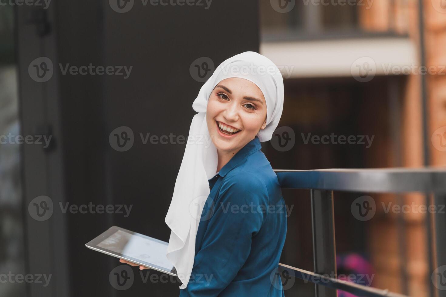 Smiling muslim girl using digital tablet, browsing Internet or social networks outdoor photo