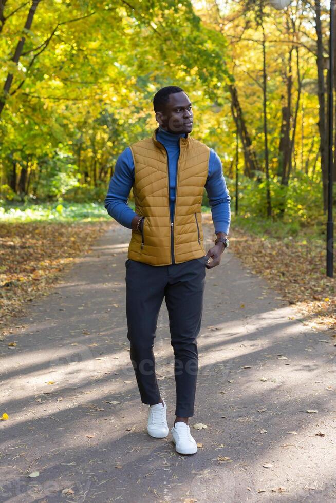 Cheerful african american young man in stylish clothes walks in autumn park on sunny warm autumn day. Concept of weekend and outdoor recreation photo