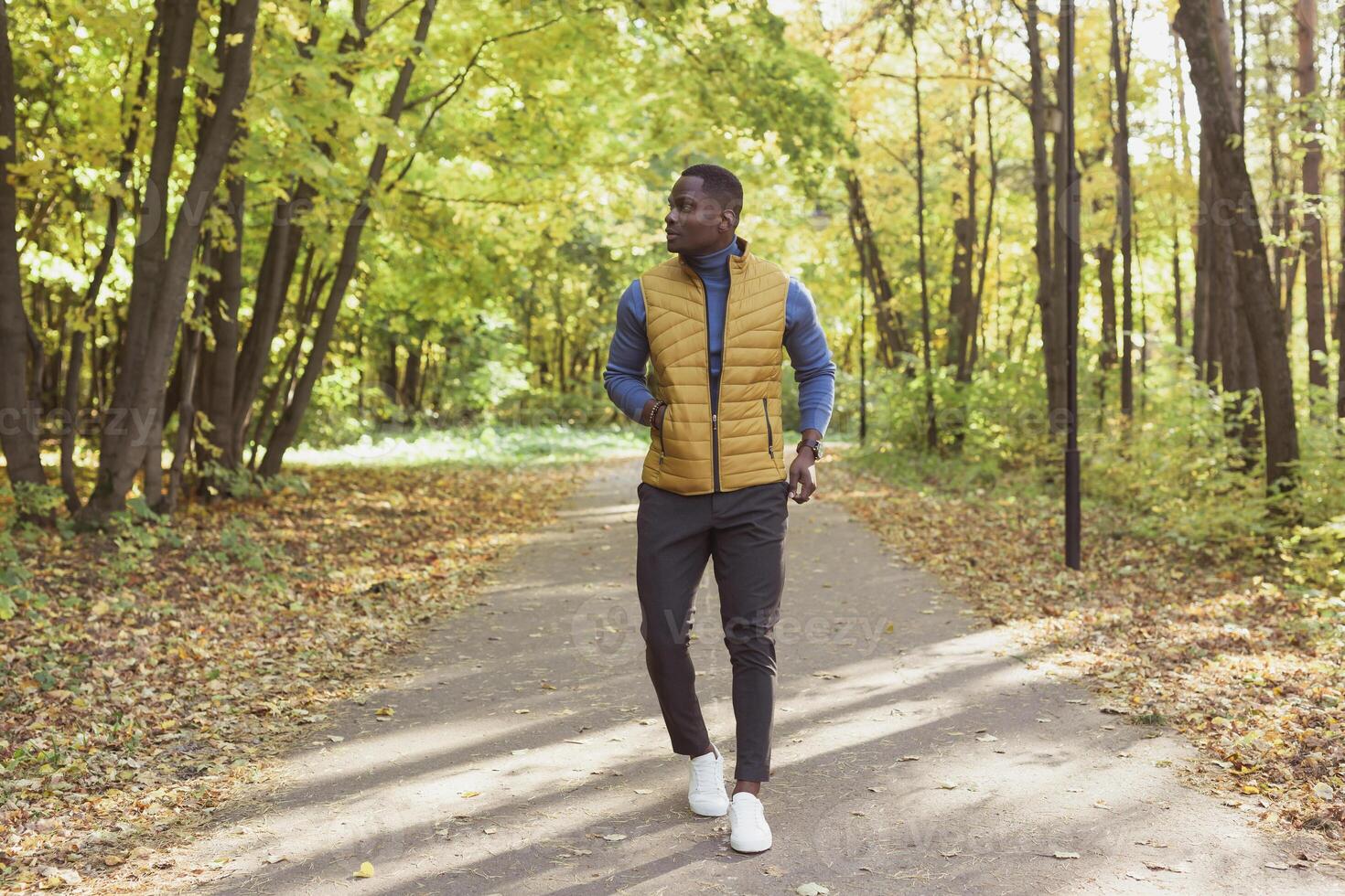 Cheerful african american young man in stylish clothes walks in autumn park on sunny warm autumn day. Concept of weekend and outdoor recreation photo
