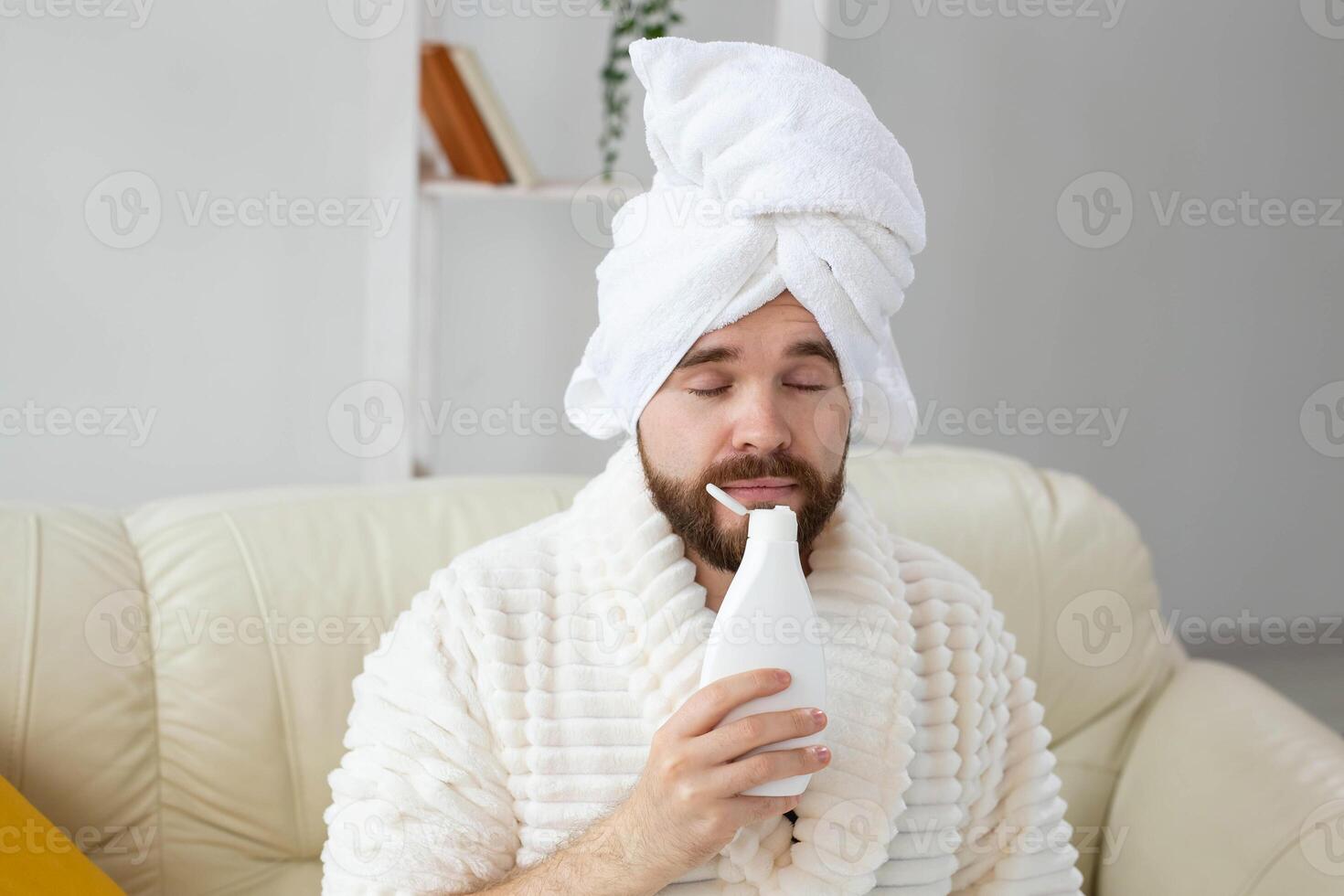 Bearded male with towel on his head applying body lotion cream. Guy smile when smell lotion cream on hand. Spa, body and skin care for man concept photo