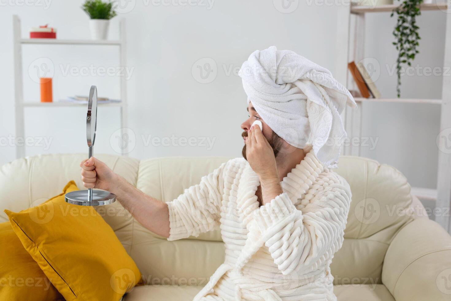 Handsome man cleaning face skin with batting cotton pads and looking at mirror. Spa, body and skin care for male concept. photo
