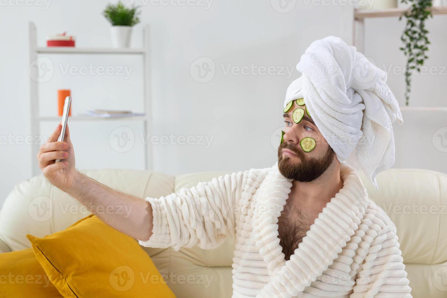 Funny bearded man enjoys with a cosmetic mask on his face made from slices of cucumber. Men skin care and spa at home concept photo