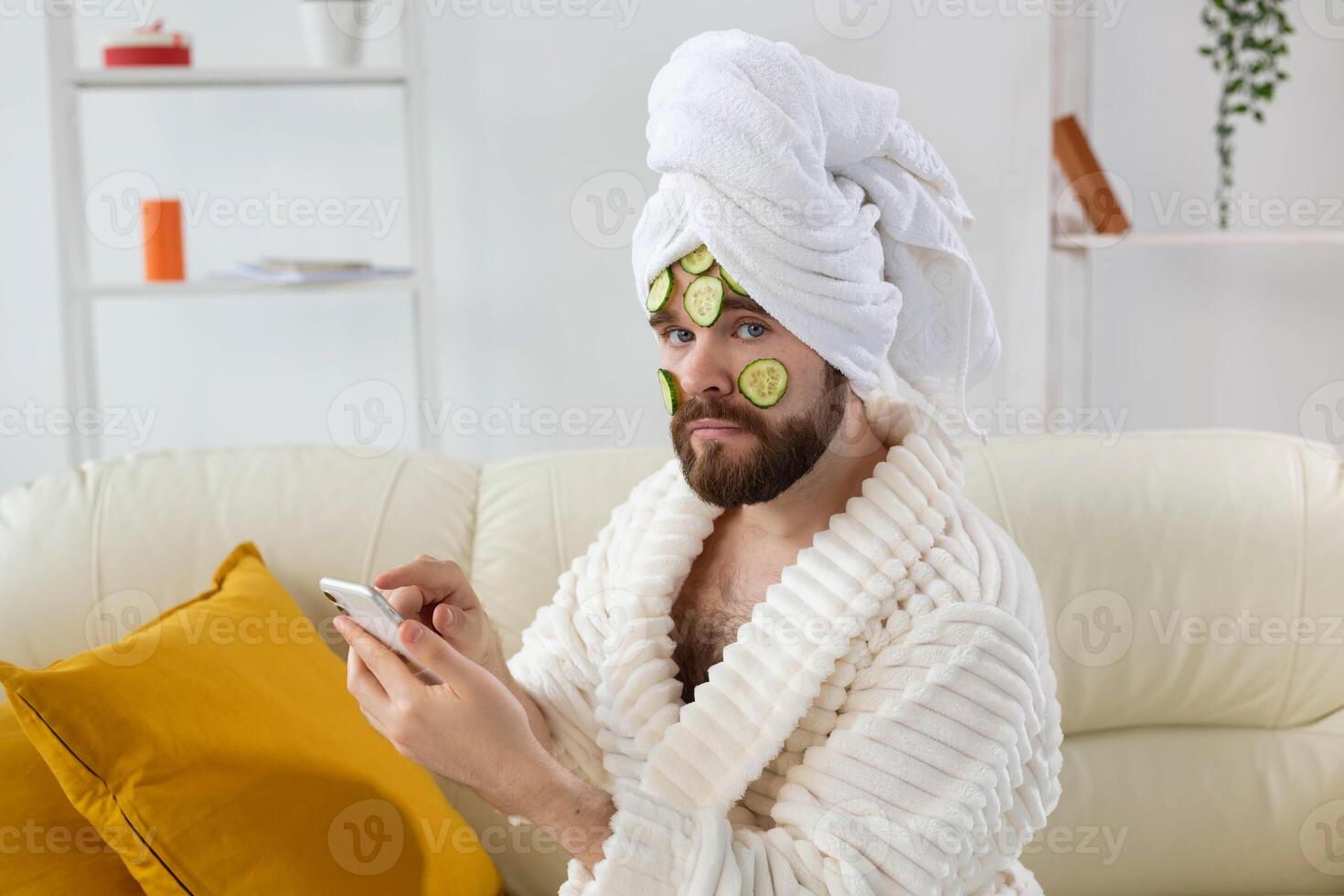 Bearded man enjoys with a cosmetic mask on his face made from slices of cucumber. Men skin care and spa at home concept photo