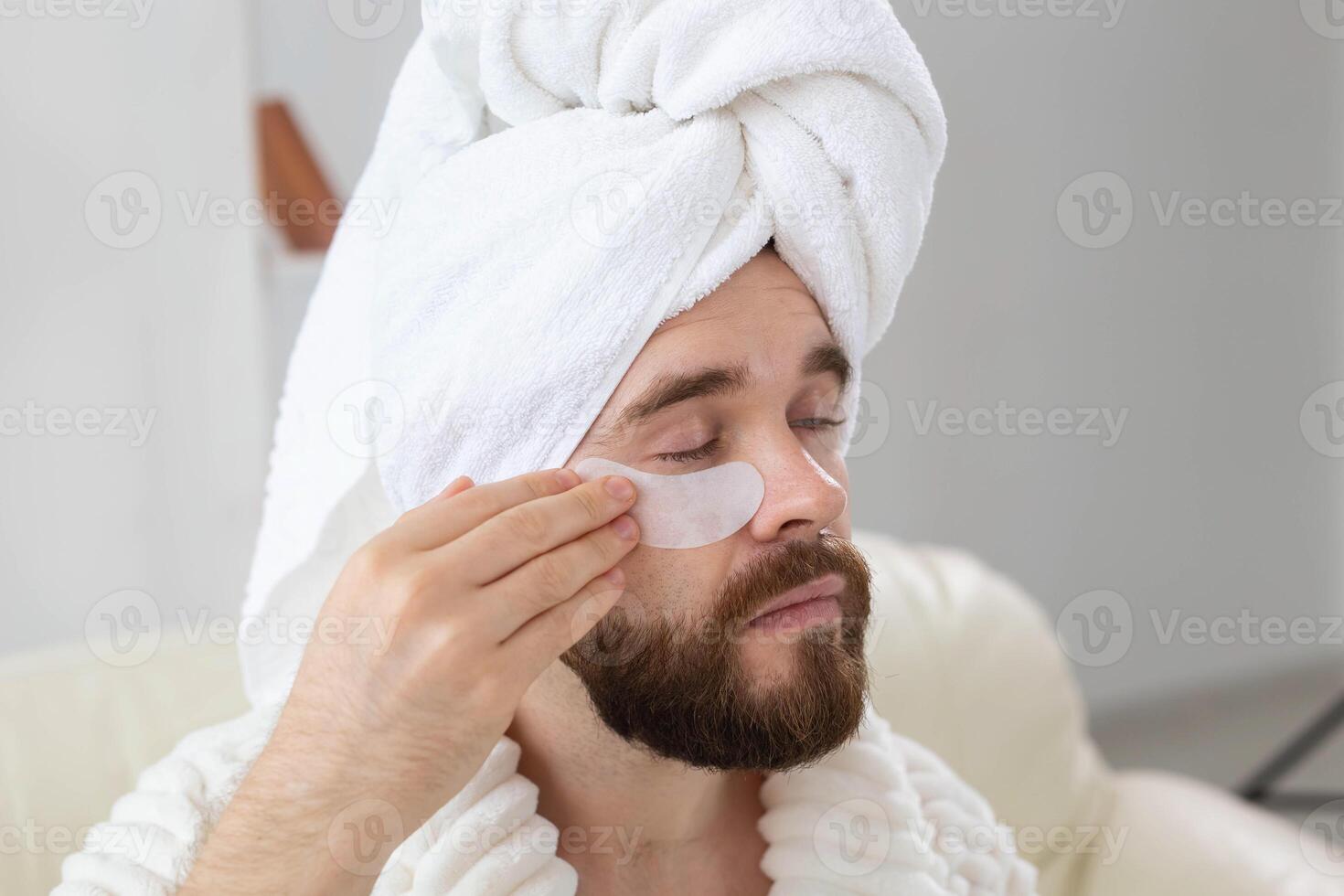 Bearded man applying eye patches on his face. Wrinkles and face home care for men. photo