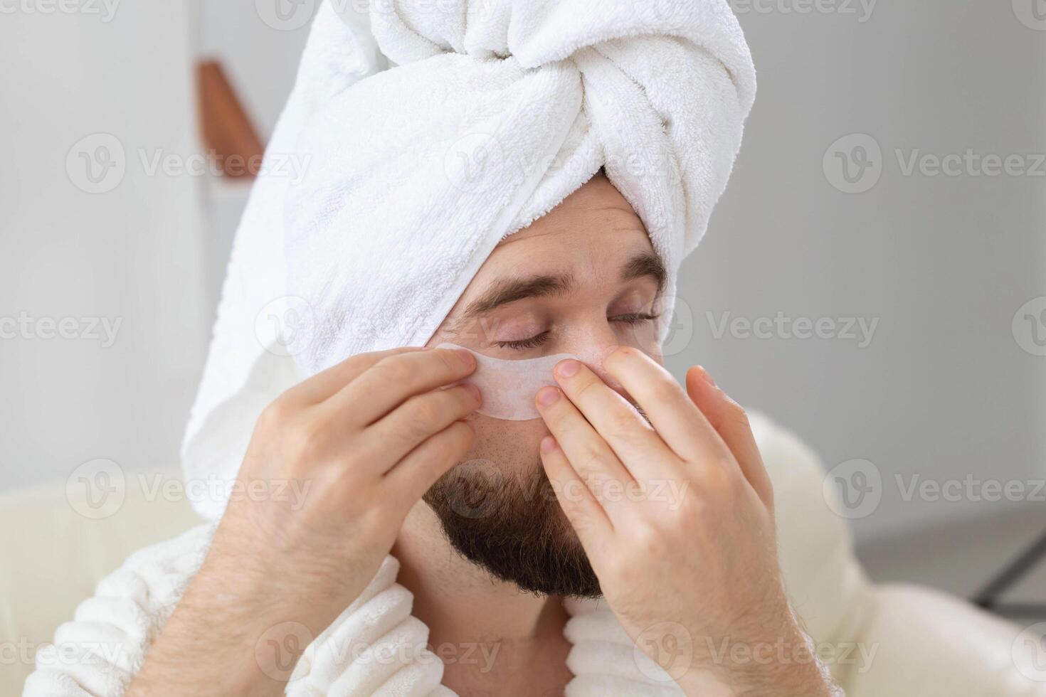 Bearded man applying eye patches on his face. Wrinkles and face home care for men. photo