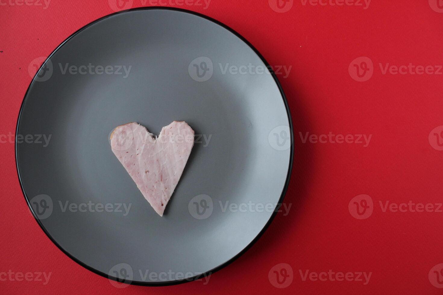 Still life breakfast for Valentine's Day Heart of ham sausage on a gray plate on a red bright background with a copy of the space photo