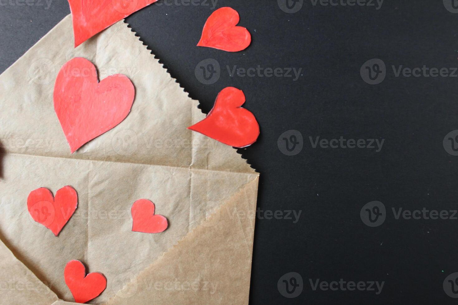 Red hearts drop out of crafting brown envelope on black background with a copy of the space photo