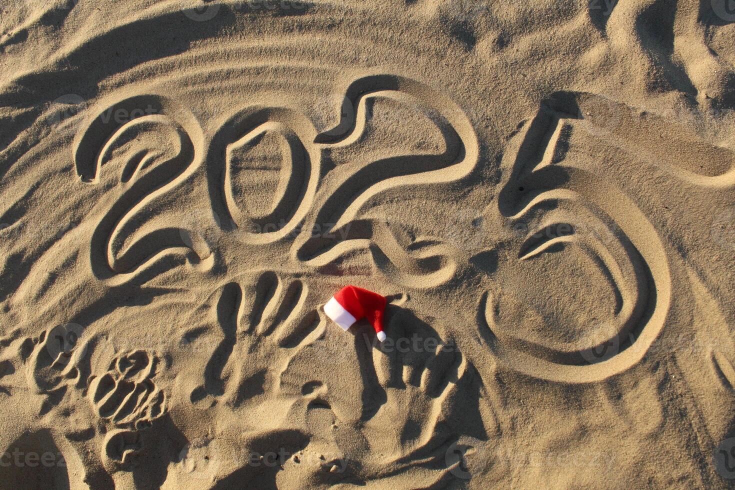 2025 The year is a digit inscription on the sand with a manta claus hat in red and white. Christmas New Year Celebration on the Sea Ocean photo