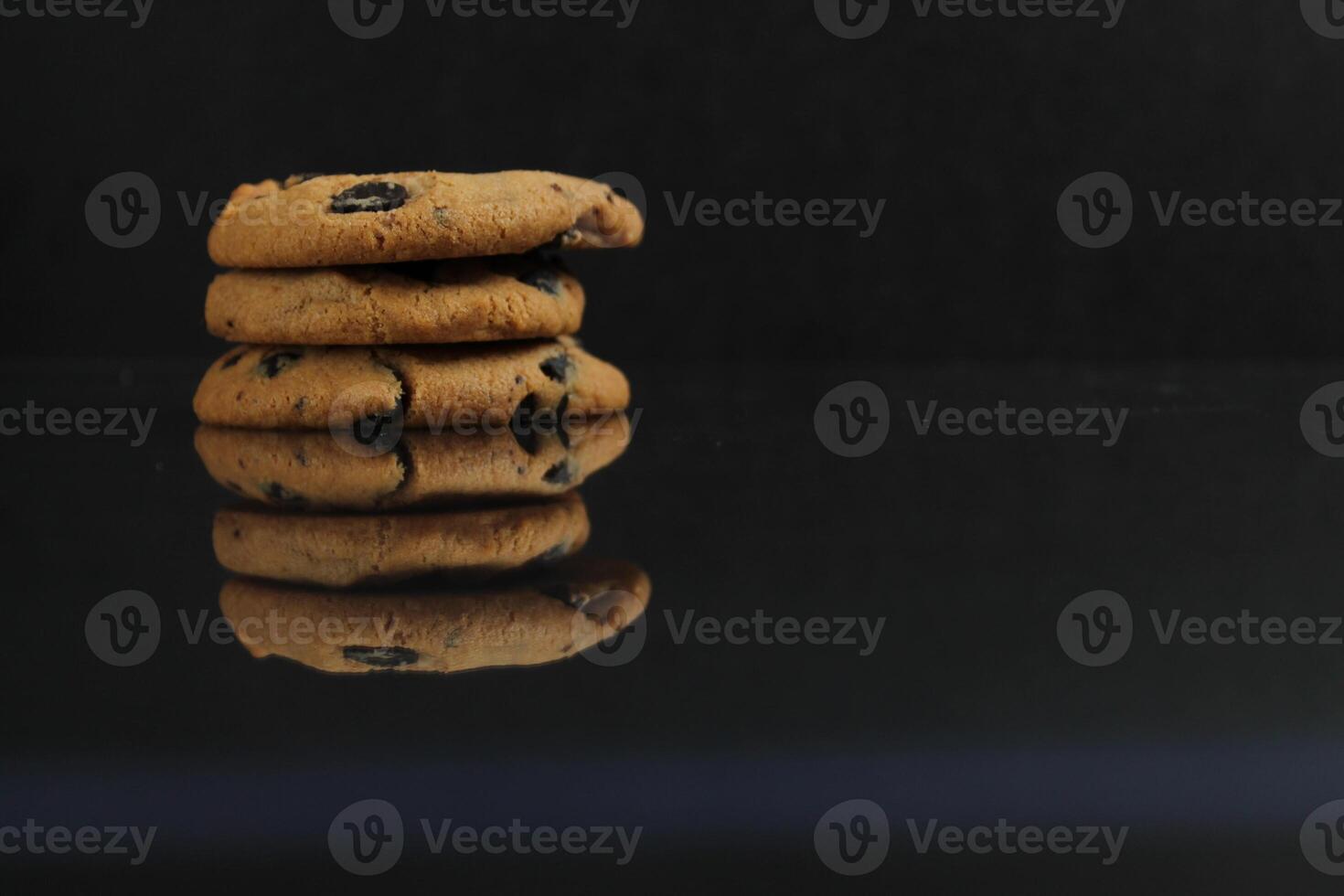 Three cookies are reflected on a black background. Optical illusion with quantities of chocolate chip cookies photo