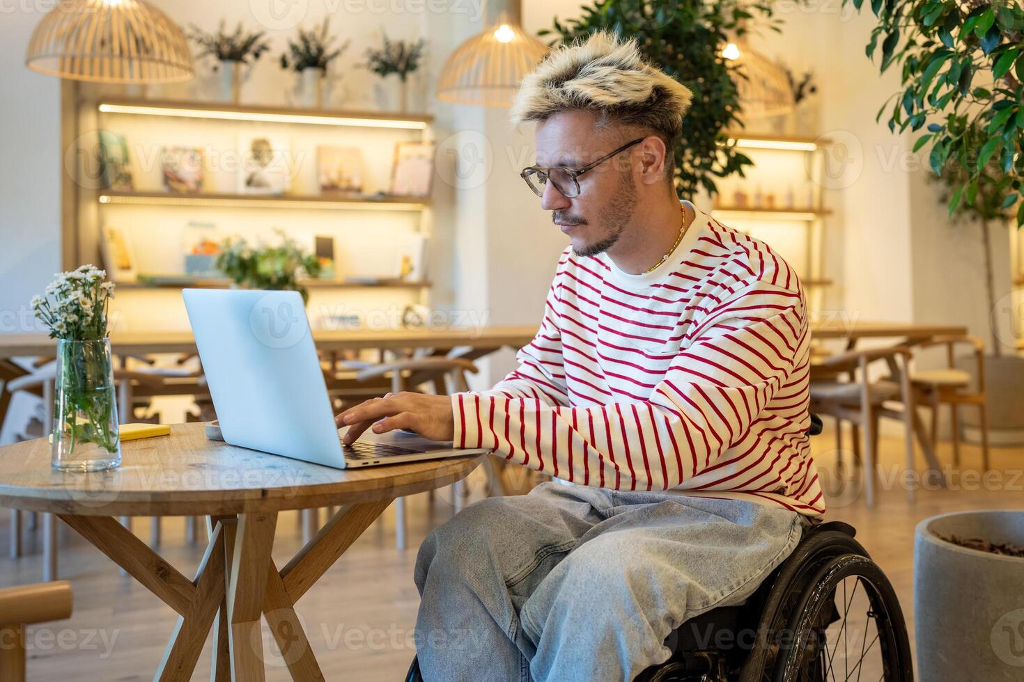 Focused disabled man in wheelchair works on laptop at cafe table. Freelancer working remotely online photo