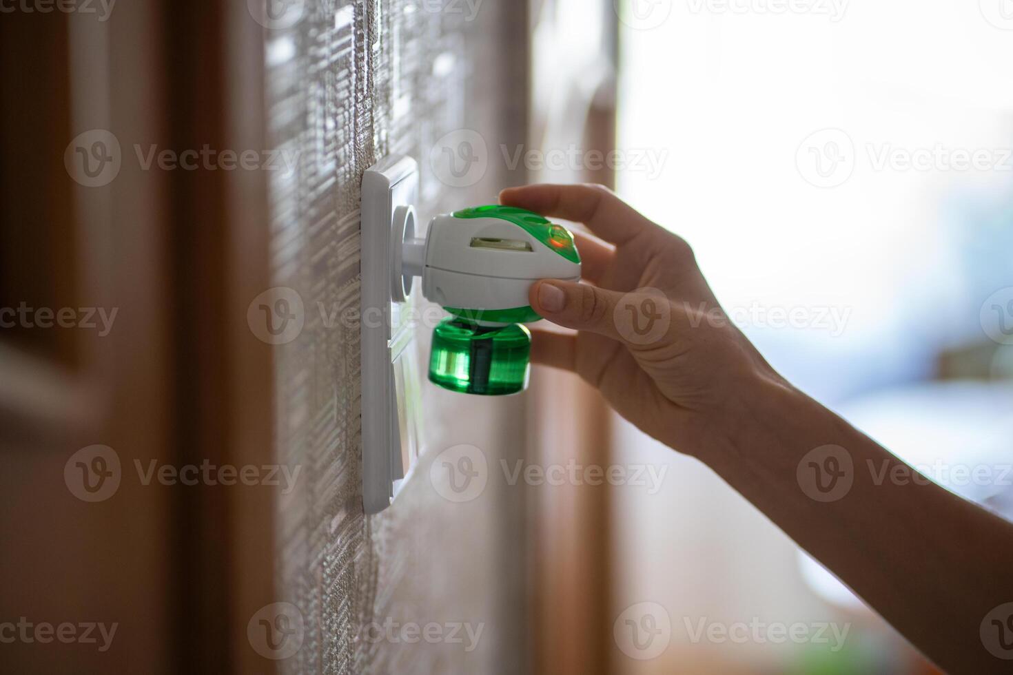 Person hand plugs mosquito repellent into the socket at home. Electric insect repellent diffuser. photo