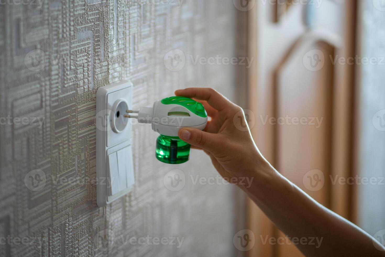 Woman hand plugs mosquito repellent into the socket at home. Electric insect repellent diffuser. photo