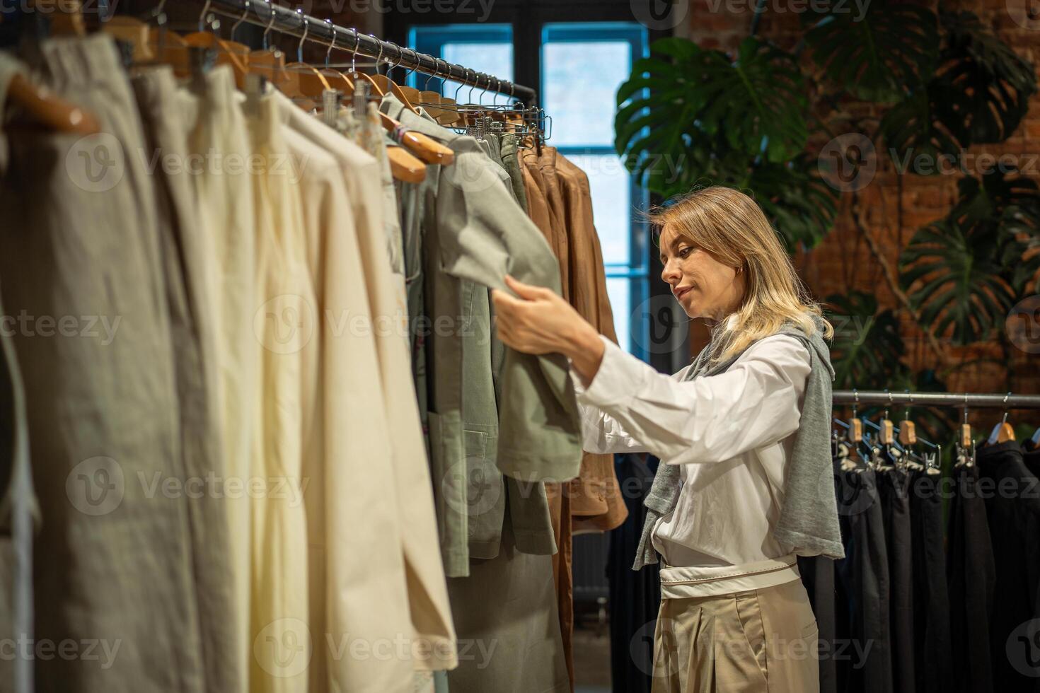 Peaceful female costumer shopping in fashion clothes boutique, choosing dresses, blouses, shirts photo