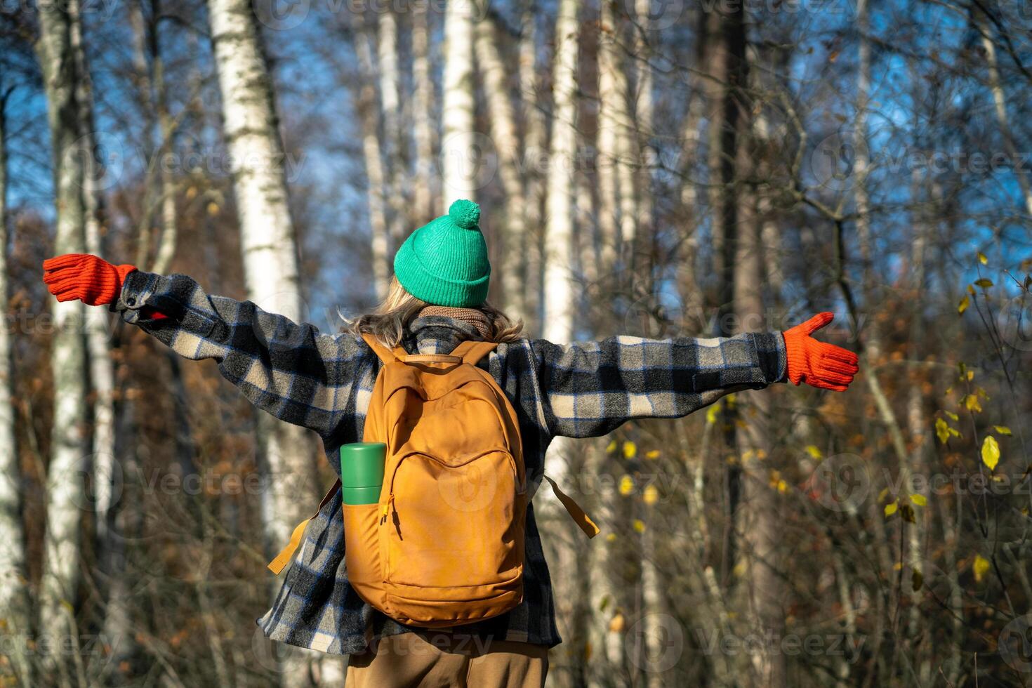 Rearview of free, happy woman with backpack spinning with arms outstretched in autumn forest photo