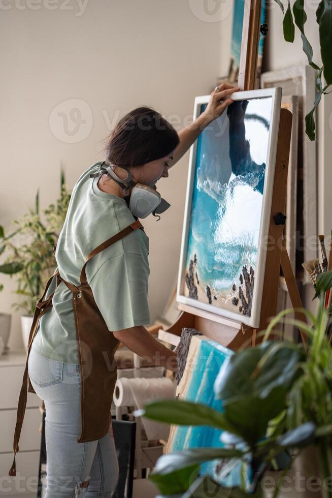 Focused artistic woman putting canvas with epoxy resin painting in liquid art technique on easel. photo