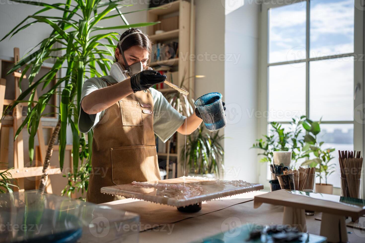 Concentrated woman, liquid artist creating pattern on canvas while working with epoxy resin painting photo