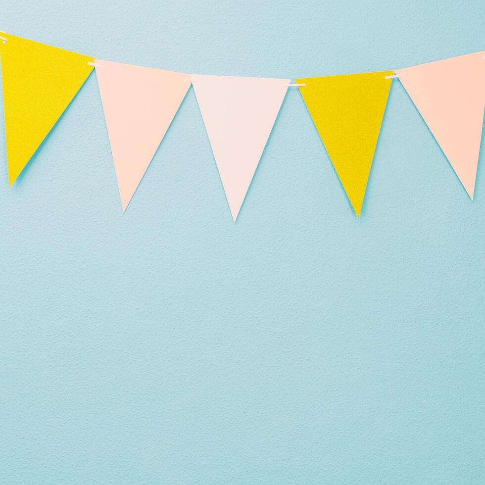 a group of yellow and pink paper flags hanging from a blue wall photo