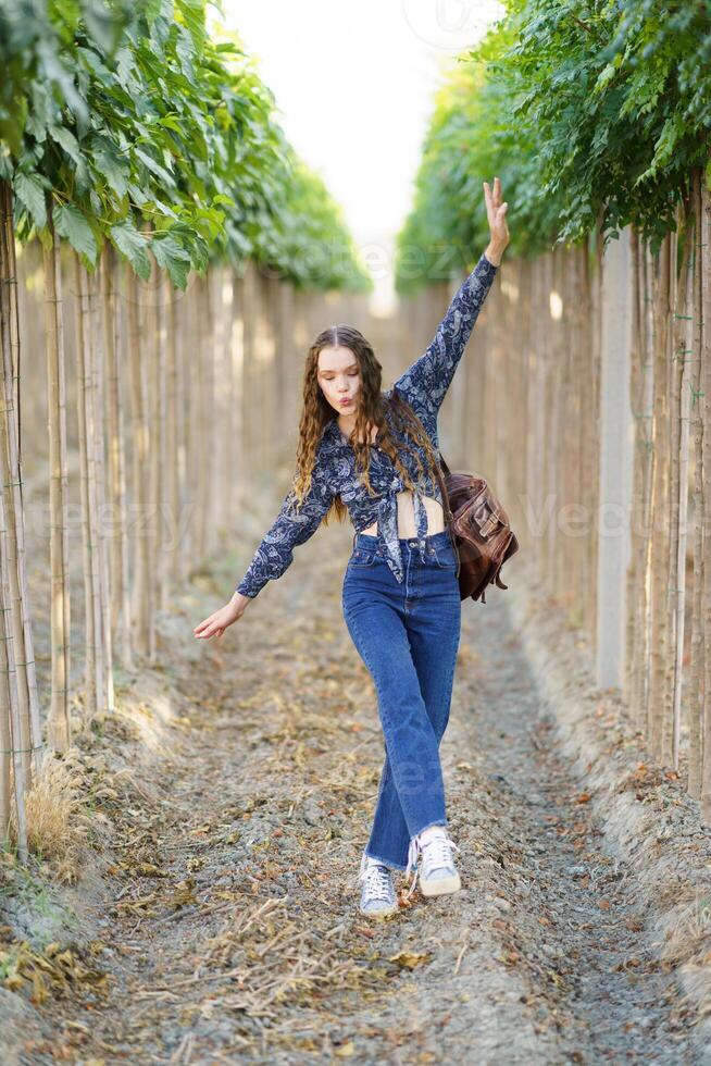 A stylish young woman dances joyfully in a scenic vineyard, surrounded by vibrant nature photo