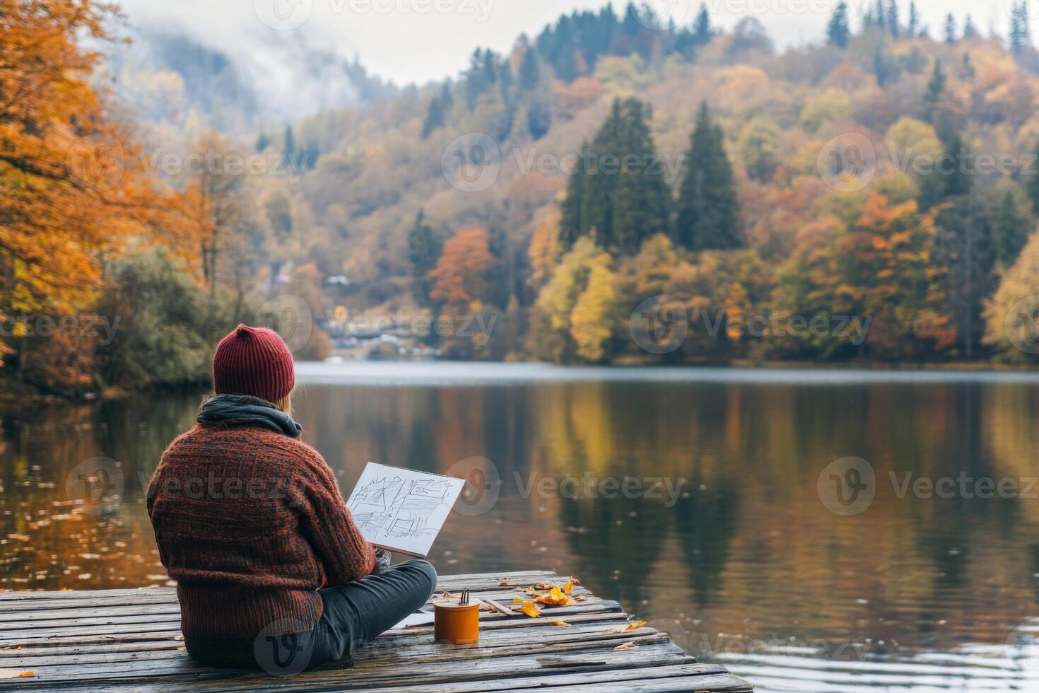 Person sketching by a lake with a view of fall foliage. photo