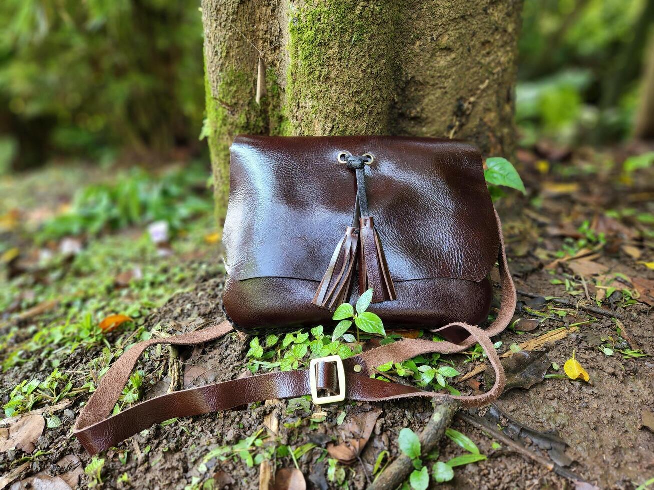 A brown leather purse sitting on the ground next to a tree photo