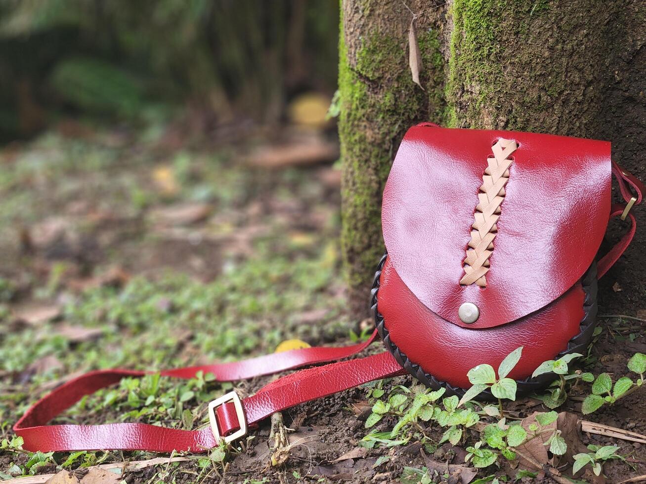 A red leather purse sitting on the ground next to a tree photo