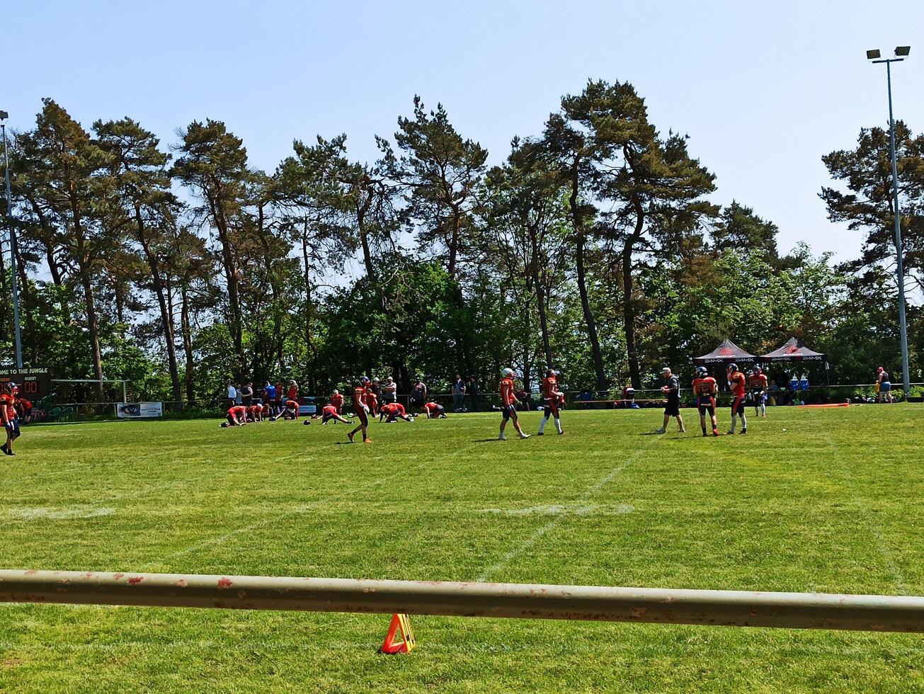 Football players compete on a sunny day in a scenic park surrounded by trees, capturing the excitement of the game in action photo