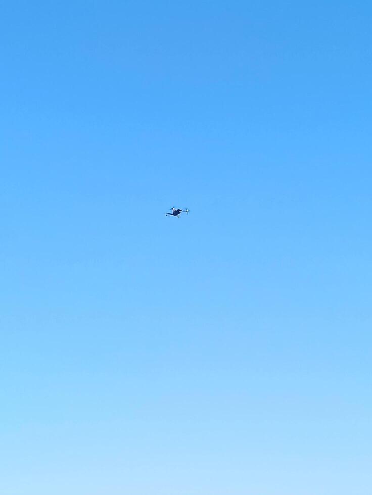 A drone hovers against a backdrop of clear blue sky, likely surveying the area or capturing images for mapping or monitoring purposes photo