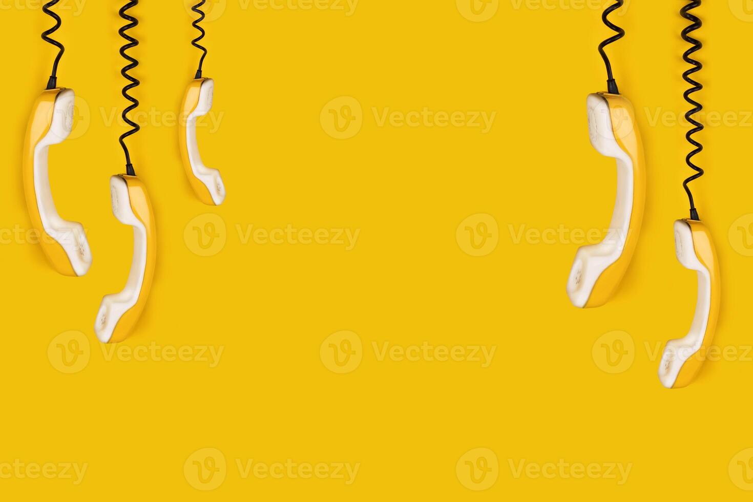 A few yellow old phone handsets dangle on wire. yellow background banner poster copy space photo