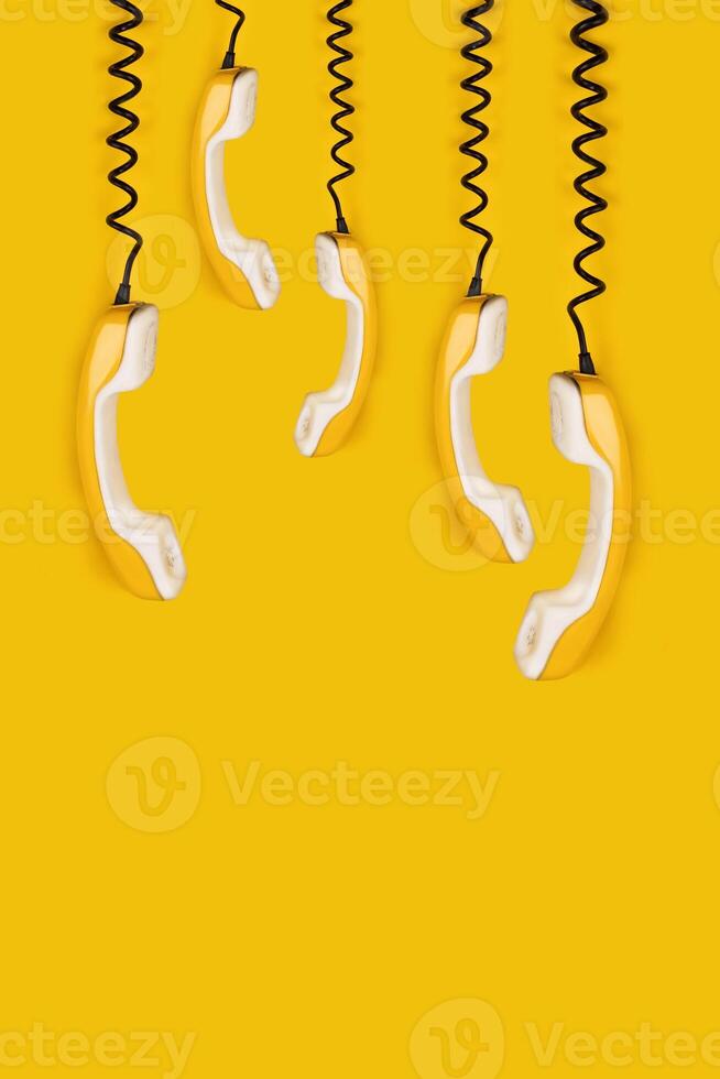 A few yellow old phone handsets dangle on wire. yellow background vertical banner poster copy space photo